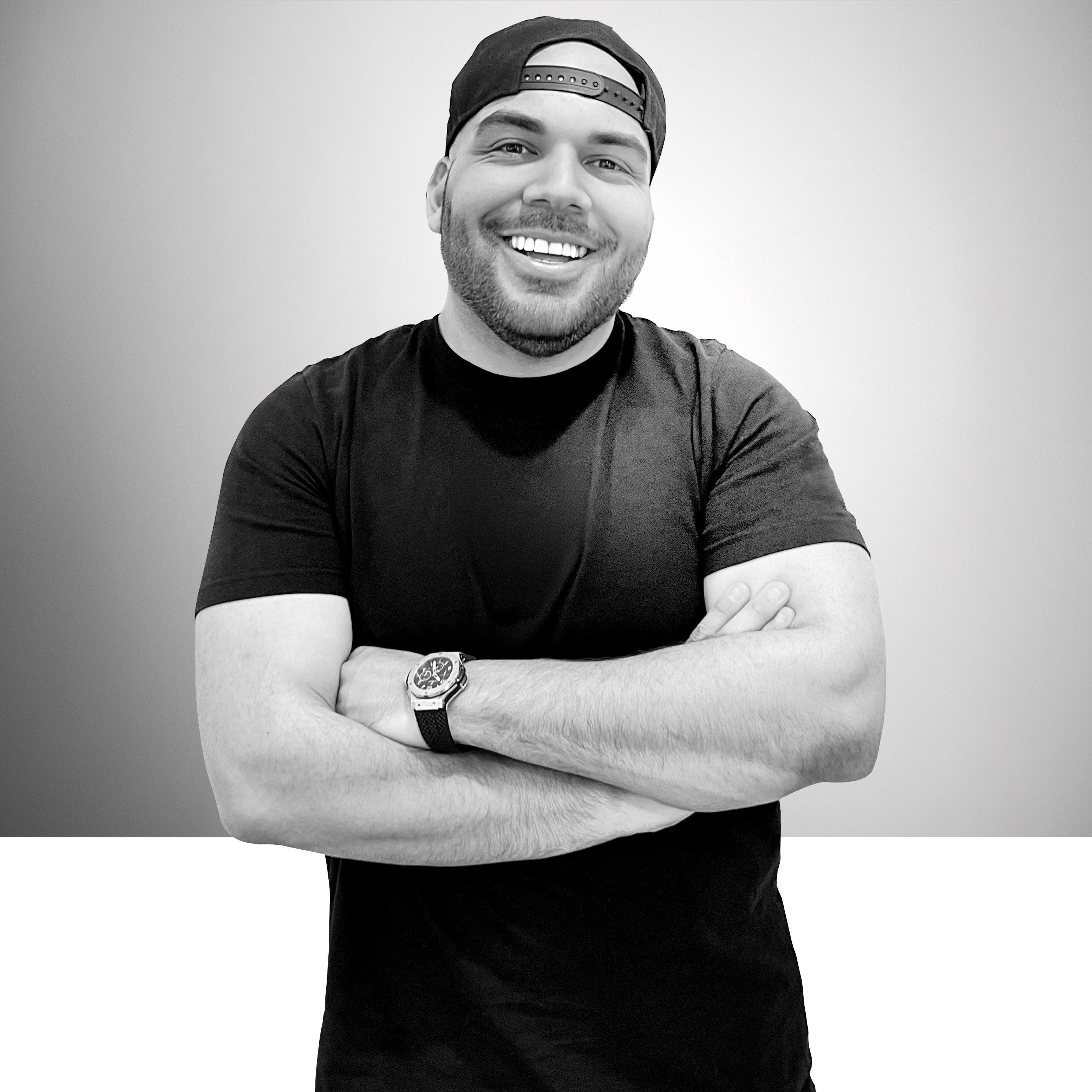 Carlos Angelucci with arms crossed in a black tee and cap