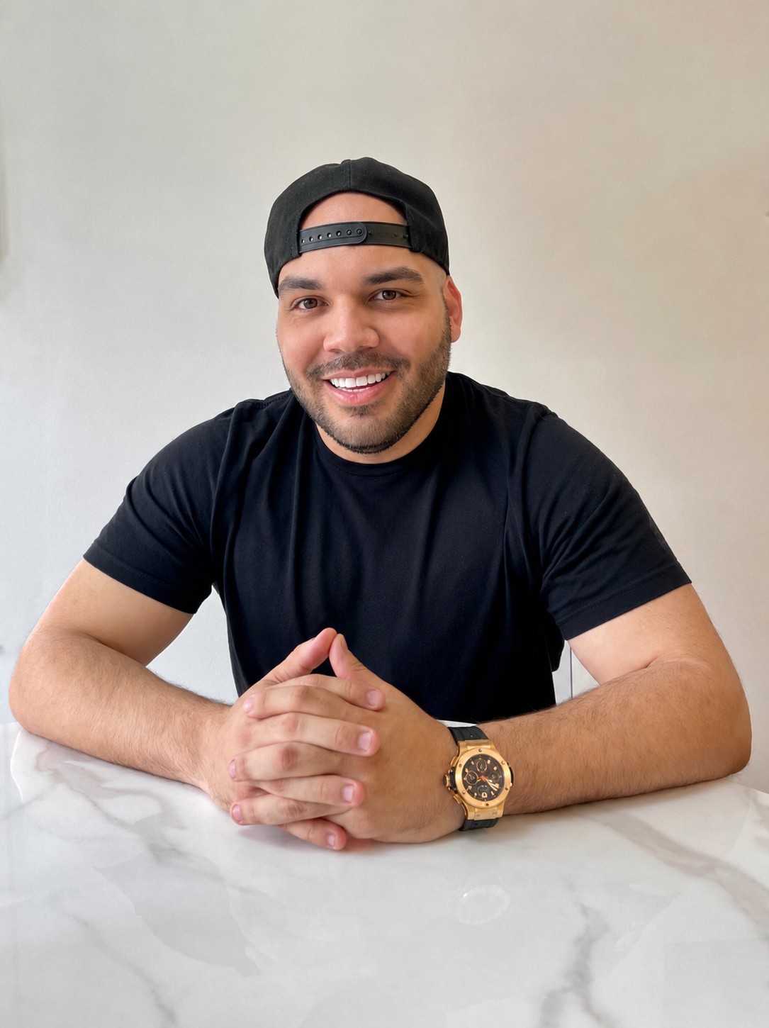 Carlos Angelucci seated at a table in a cap and black tee