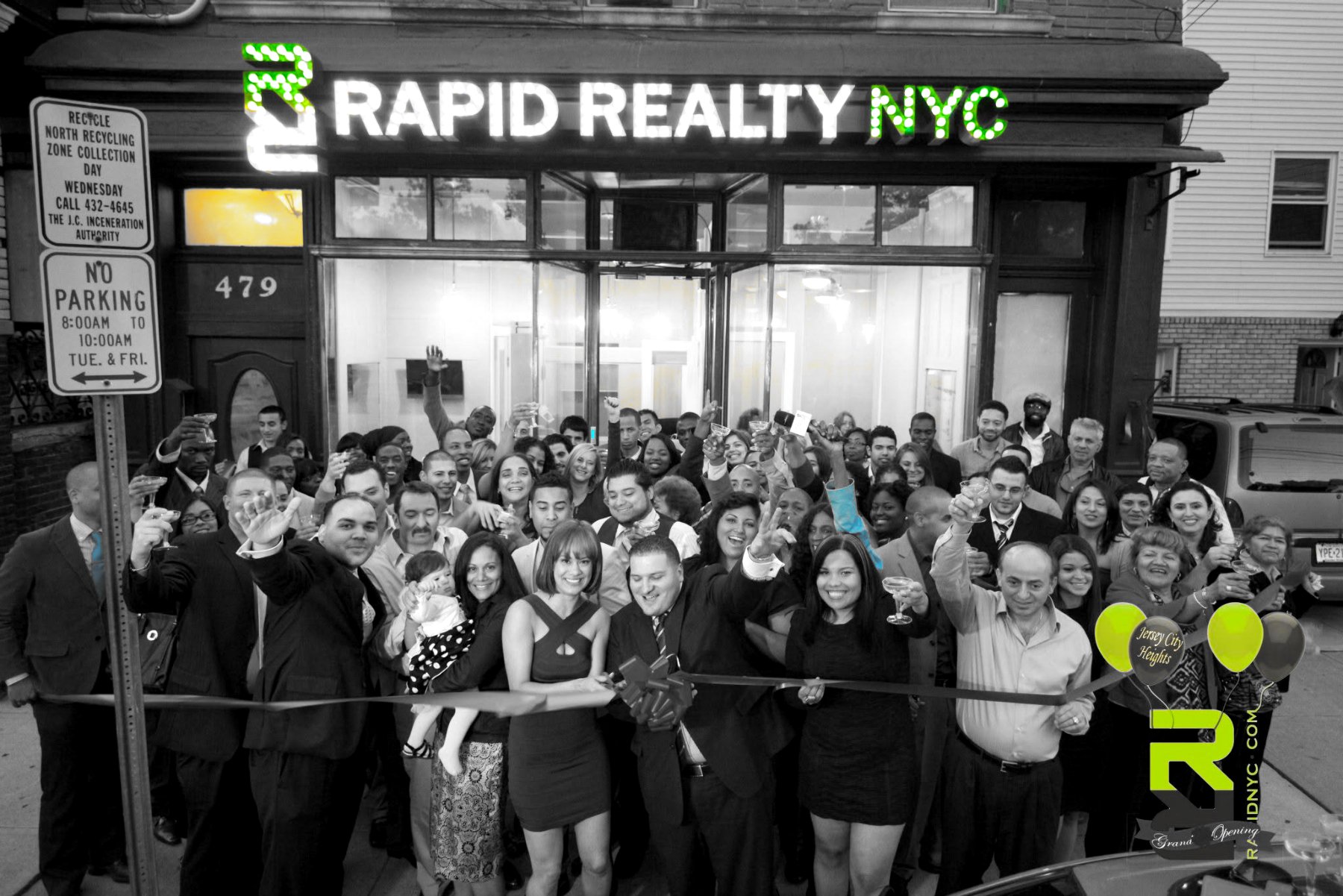 Rapid Realty NYC franchise grand opening — agents, family and neighbours on the sidewalk under a lit storefront sign